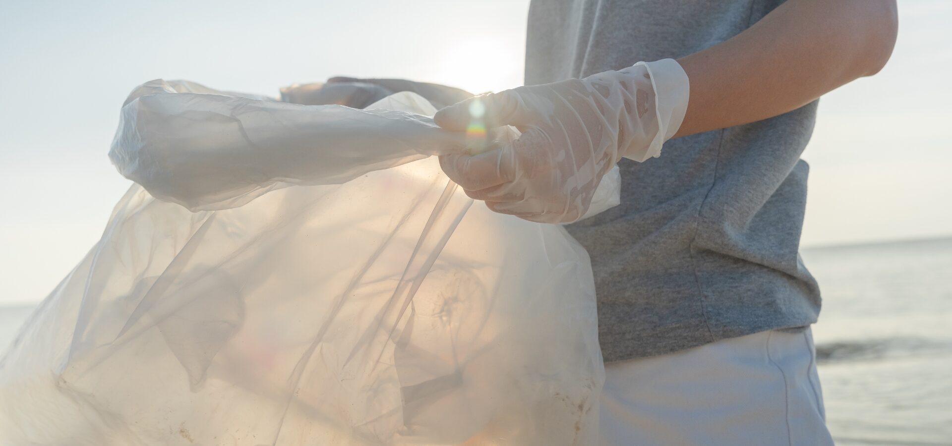 Eine Person in T-Shirt steht am Strand und hält einen leeren Müllbeutel.